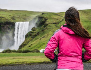 Woman traveler at beautiful scenery of the majestic Skogafoss Waterfall in countryside of Iceland in summer. Skogafoss is the top famous natural landmark and tourist attraction of Iceland and Europe.